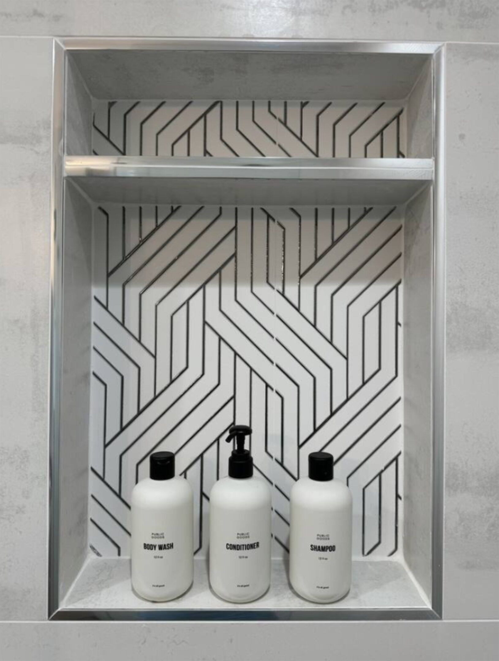 Un estante de baño con tres botellas de artículos de tocador etiquetadas como 'BODY WASH', 'CONDITIONER' y 'SHAMPOO'.
