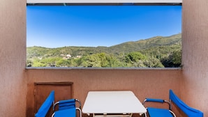 Un balcon avec une table et deux chaises, donnant sur un paysage montagneux verdoyant, parsemé de bâtiments.