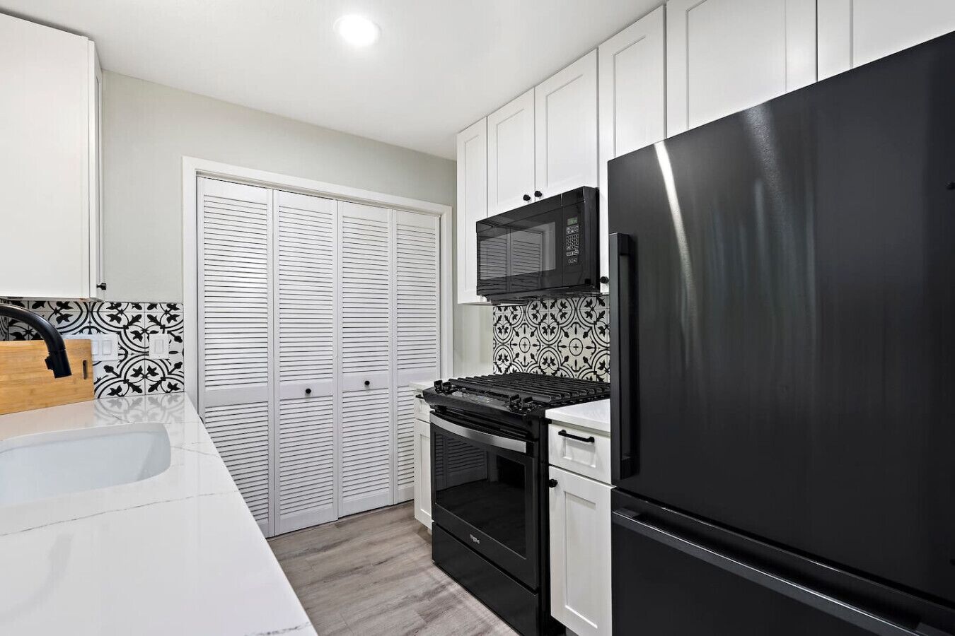 A modern kitchen with white cabinets, a black refrigerator, a microwave, and a stove.