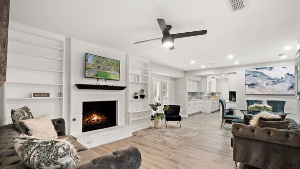 A spacious living room with a fireplace, a ceiling fan, and a large painting on the wall.