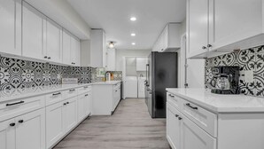 A modern kitchen with white cabinetry, patterned backsplash, and a stainless steel refrigerator.