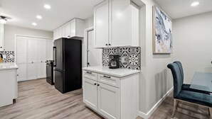 A modern kitchen with white cabinetry, a black refrigerator, and a coffee maker on the counter.