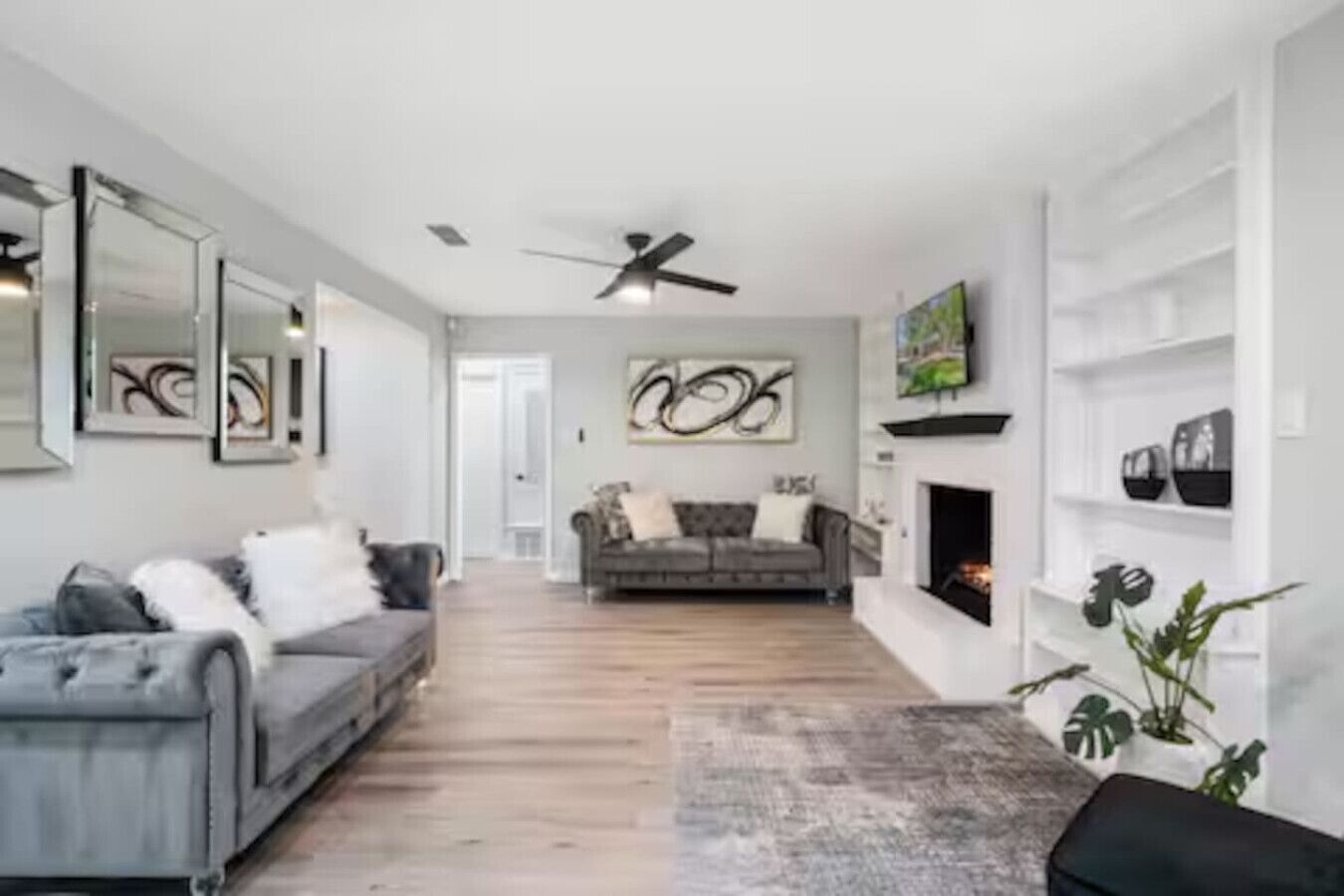 Ein modernes Wohnzimmer mit einem grauen Sofa, einem Kamin und einem Deckenventilator.