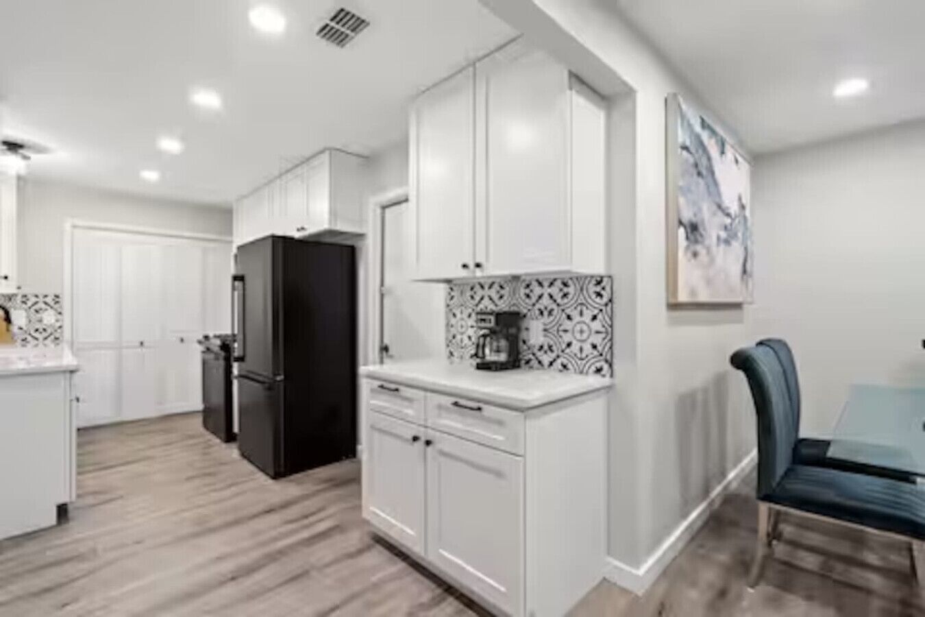A modern kitchen with white cabinetry, a black refrigerator, and a coffee maker on the counter.
