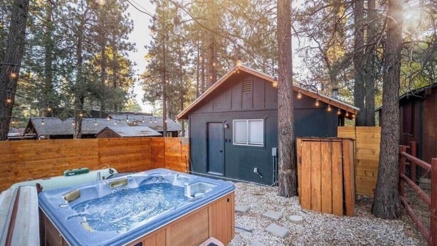 A hot tub in a wooded backyard with a wooden deck and a small shed. - Black Diamond Retreat Designer Cabin Hot Tub (Big Bear)