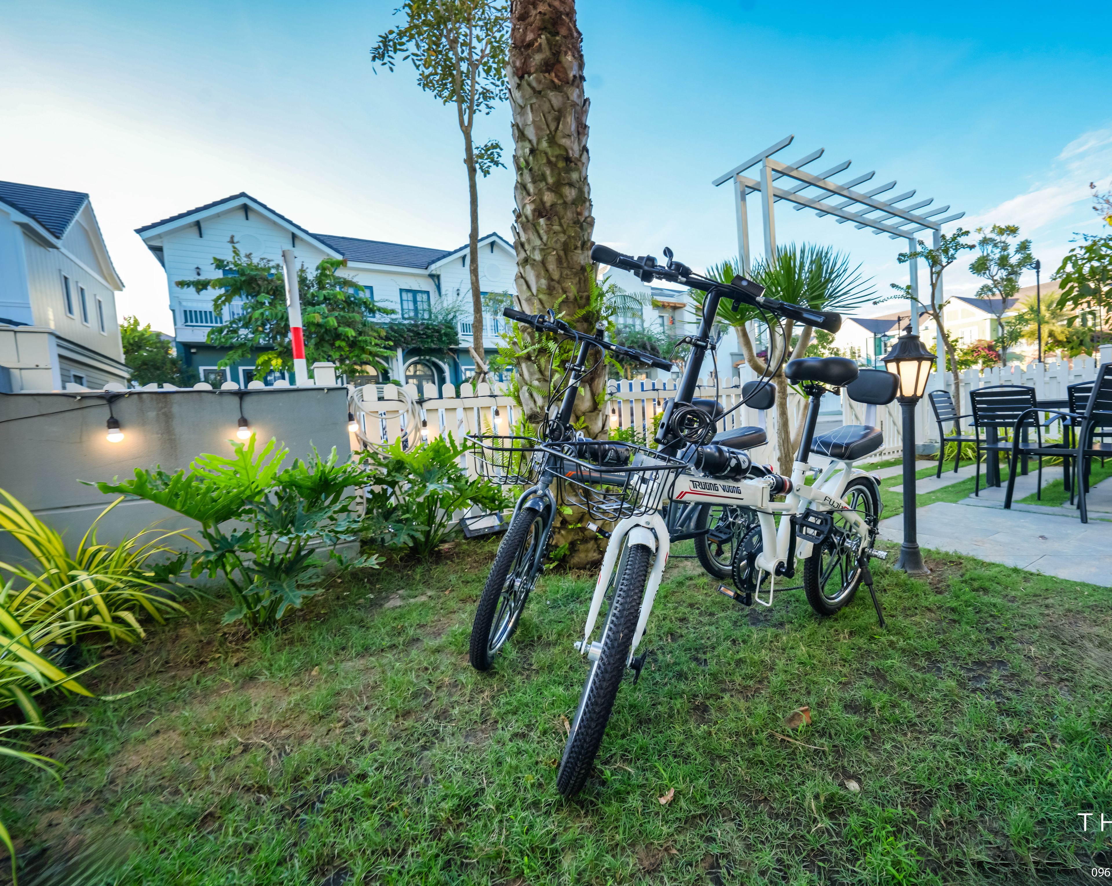 Una bicicleta blanca estacionada en un área con césped, una pérgola y asientos al aire libre.