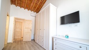 A hallway with wooden flooring, white walls, and a wooden ceiling. There are two wooden doors, a white dresser with drawers, and a flat-screen TV mounted on the wall. - Appartamento Lentisco - Lentisco (Portoferraio)