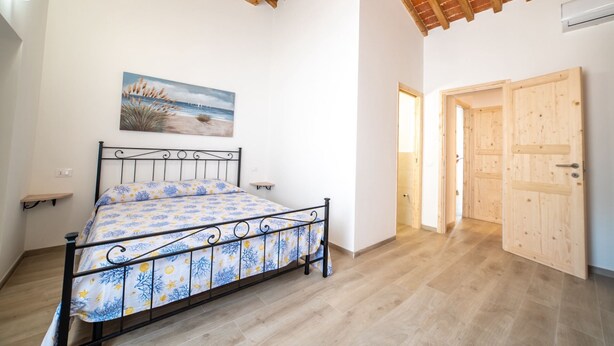 A bedroom with a bed, a painting, and a wooden door. - Appartamento Lentisco - Lentisco (Portoferraio)