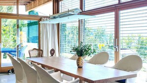 Uma sala de jantar moderna com uma mesa comprida, cadeiras brancas e um vaso de flores.
