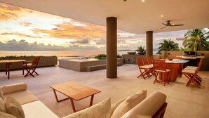 Un vaste espace extérieur avec vue sur la mer, comprenant une table en bois, des chaises, un canapé et un barbecue.