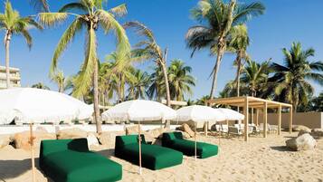 A beachside lounge area with green cushioned seating, white umbrellas, and palm trees.
