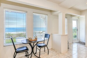 A dining area with a table and chairs, large windows with blinds, a view of the sea, and a white tiled floor. - Spacious Beachfront House, Breathtaking Ocean Views, Near Historic Attractions, $300 in Free Tickets (St. Augustine)