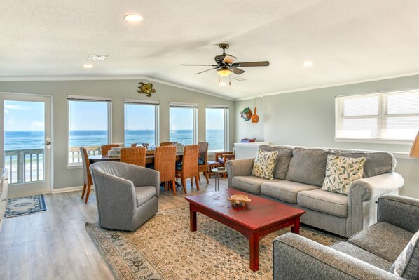A spacious living room with a view of the ocean, a ceiling fan, and a dining area with chairs and a table. - Spacious Beachfront House, Breathtaking Ocean Views, Near Historic Attractions, $300 in Free Tickets (St. Augustine)