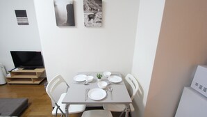 A dining area with a table set for four, white chairs, a small potted plant, and artwork on the wall. - Small-Town Feel, Big-City Access | Homey Stay in Nakano (中野区野方)