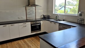Uma cozinha moderna com armários brancos, bancada preta, forno de aço inoxidável, pia e janela com vista para o verde.