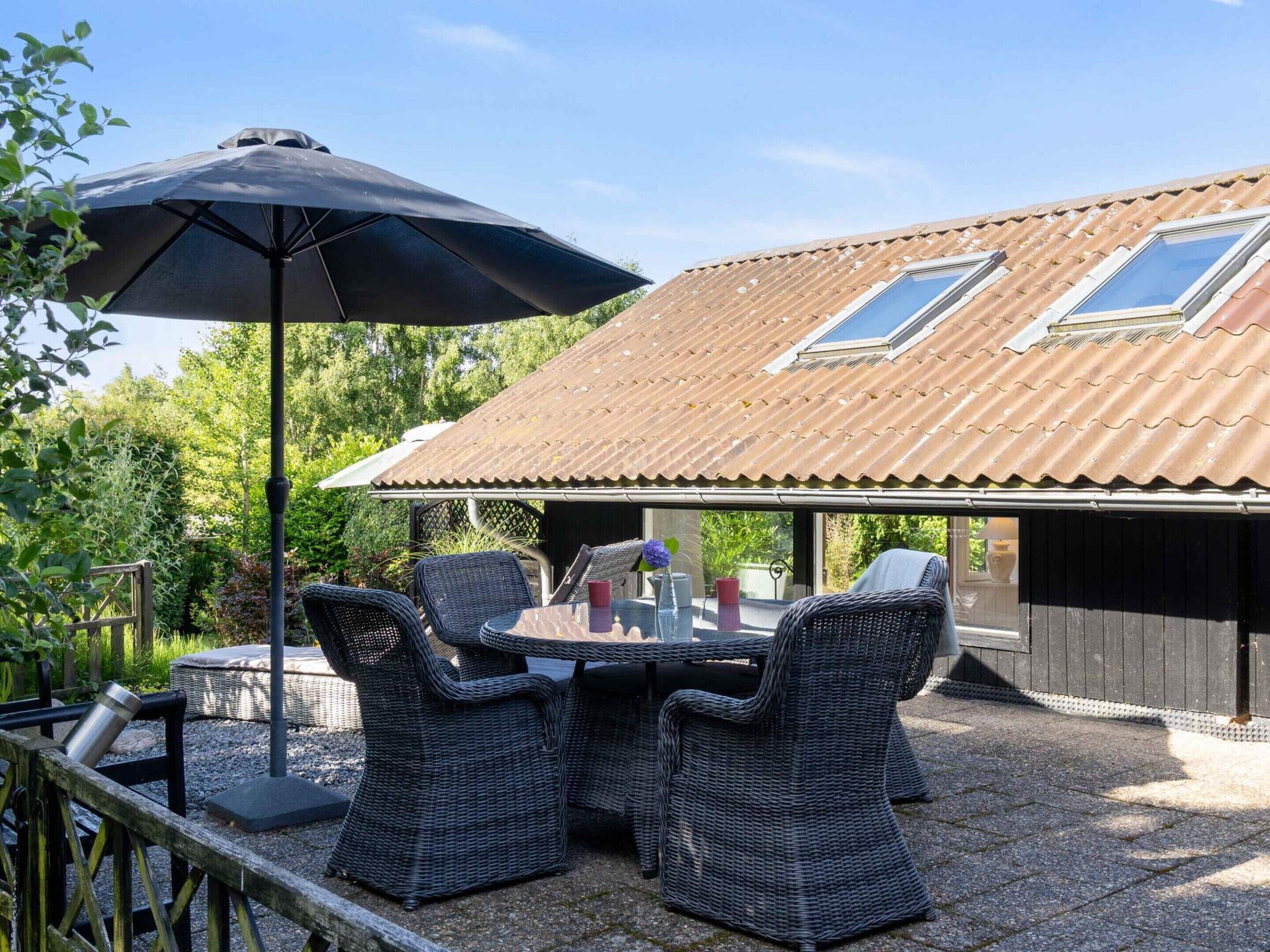 Eine Außenpatio mit Korbmöbeln, einem Tisch und einem Sonnenschirm. Im Dach befinden sich zwei Oberlichter.