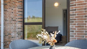 A patio with wicker chairs, a round table, and a vase with flowers. - 10 Person Holiday Park Home in Ulfborg (Ulfborg)
