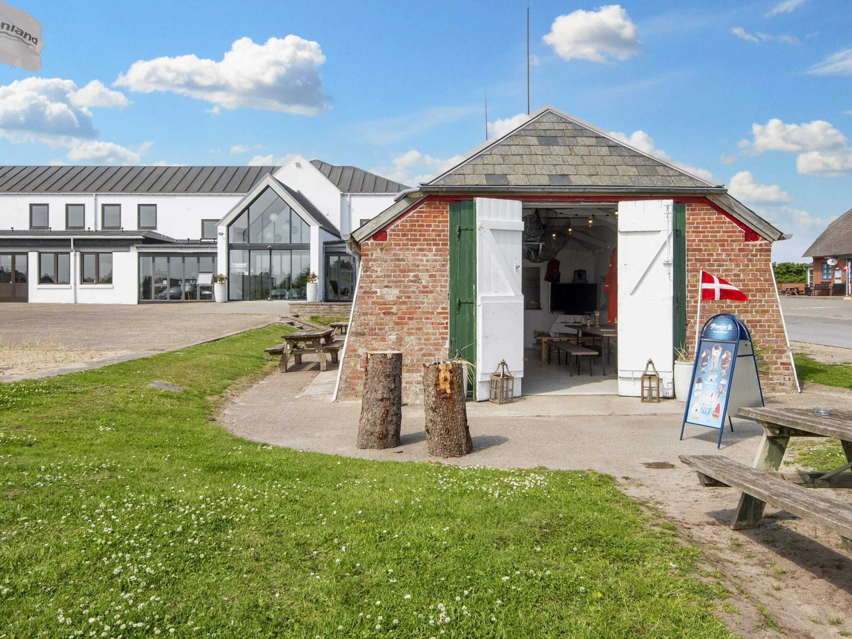 A small brick building with a green door and a flag, a picnic table, and a signboard.