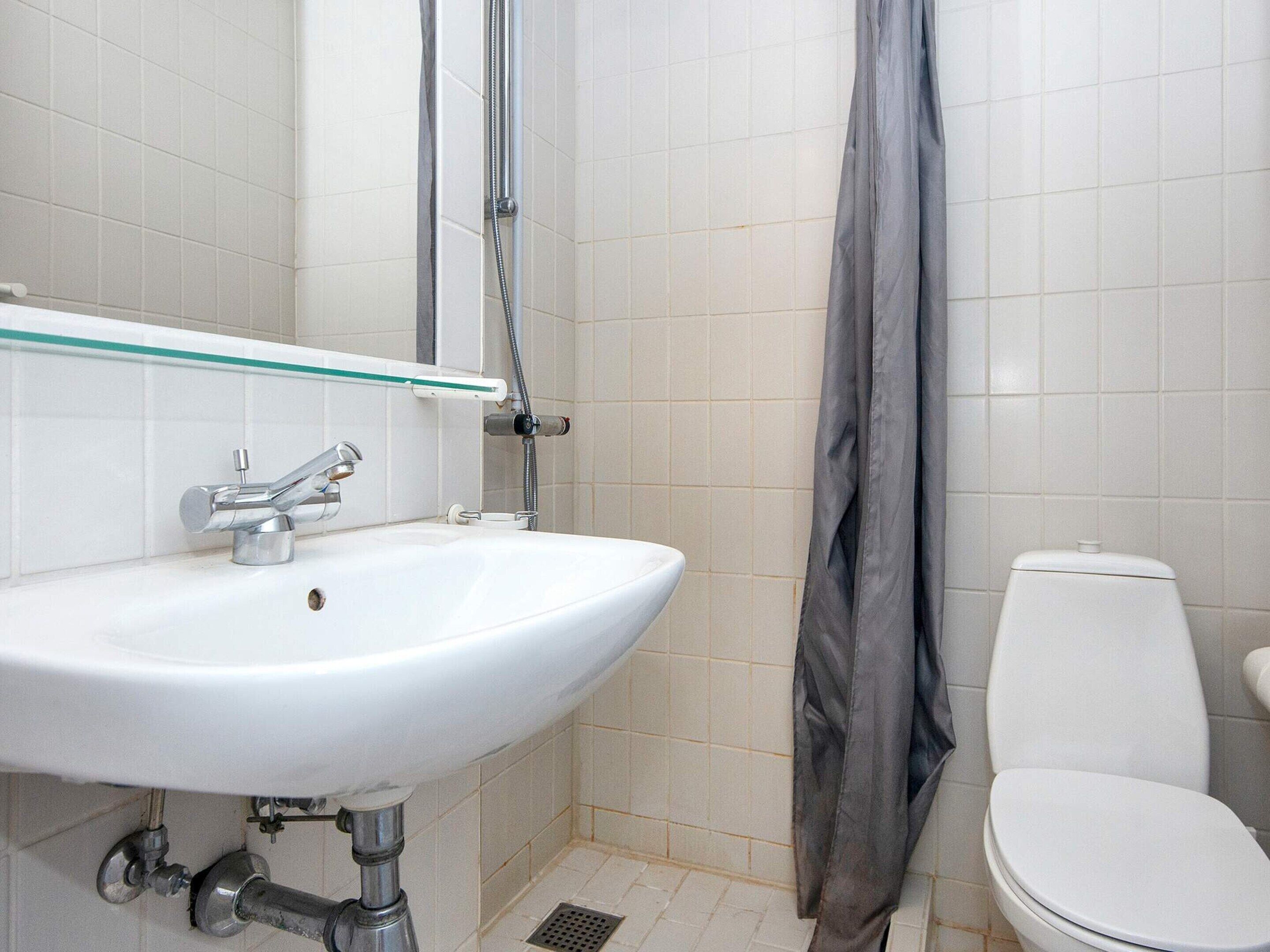 A bathroom with a white sink, a glass shelf, a shower curtain, and a toilet.