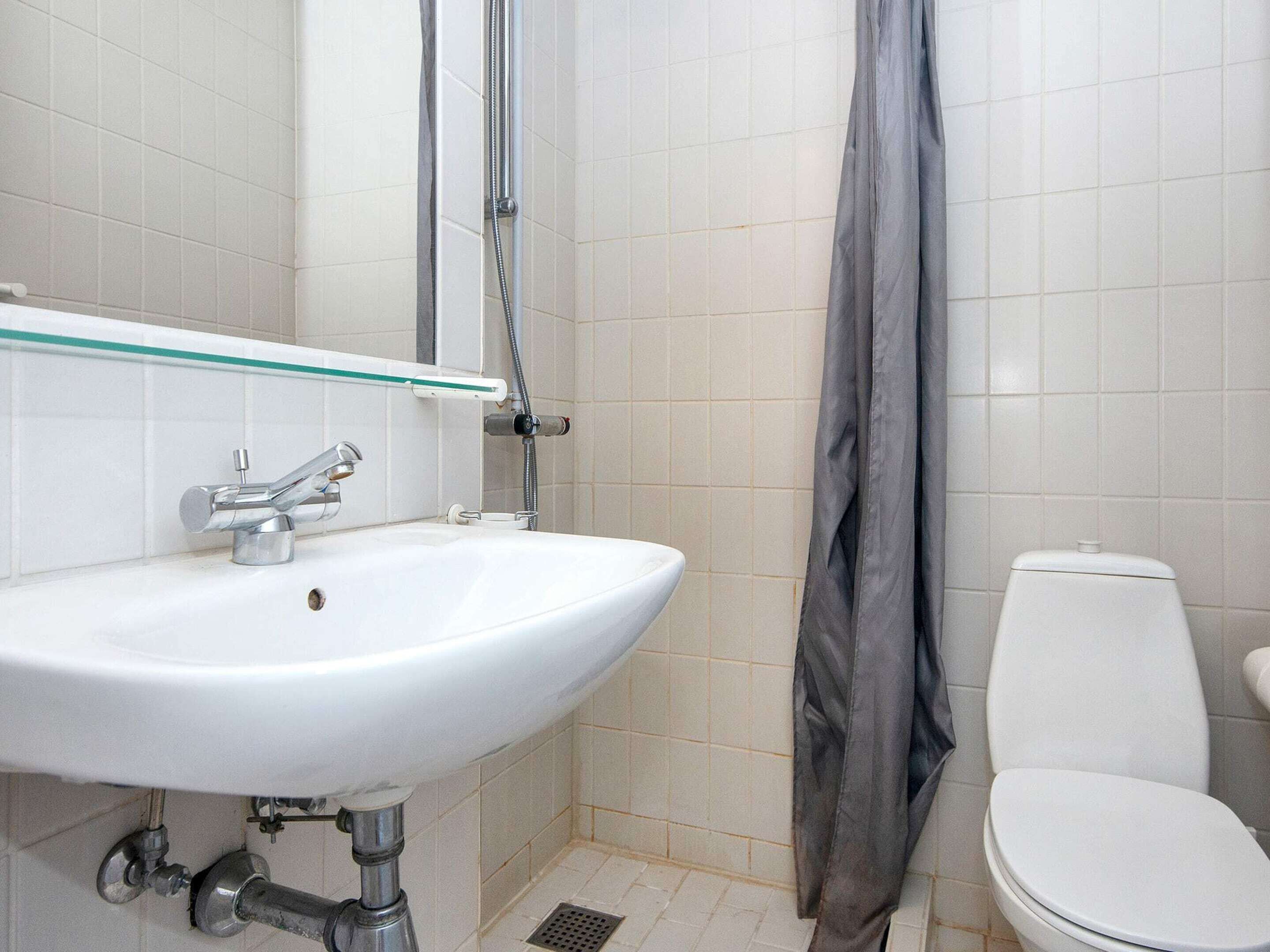 Une salle de bain avec un lavabo blanc, une étagère en verre, un rideau de douche et des toilettes.