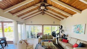 Un ampio soggiorno con alto soffitto in legno, un tavolino da caffè in vetro e un divano beige con cuscini rossi.