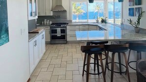Una cucina moderna con mobili bianchi, un'isola centrale e vista sull'oceano.