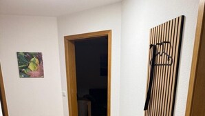 En hall med ett grått mattgolv, en träbänk och en väggmonterad hylla.