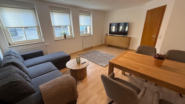 Ett modernt vardagsrum med en soffgrupp, ett matbord i trä och en tv-apparat placerad på ett träskåp.
