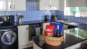Een moderne keuken met witte kasten, blauwe tegels, een wasmachine, een broodrooster en een mand met lekkernijen.