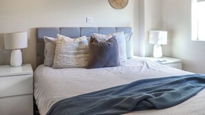 Een keurig opgemaakt slaapkamer met een bed, twee nachtkastjes en een wandlamp.