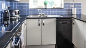 Een moderne keuken met een zwart aanrecht, witte kasten, een ingebouwde vaatwasser en een raam met uitzicht op groen.