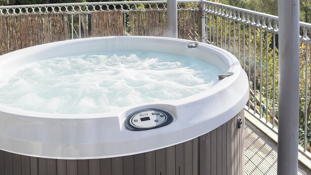 Een bubbelbad op een terras met uitzicht op een bebost landschap.
