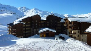 Un hotel de varios pisos con tejado cubierto de nieve, con montañas al fondo.