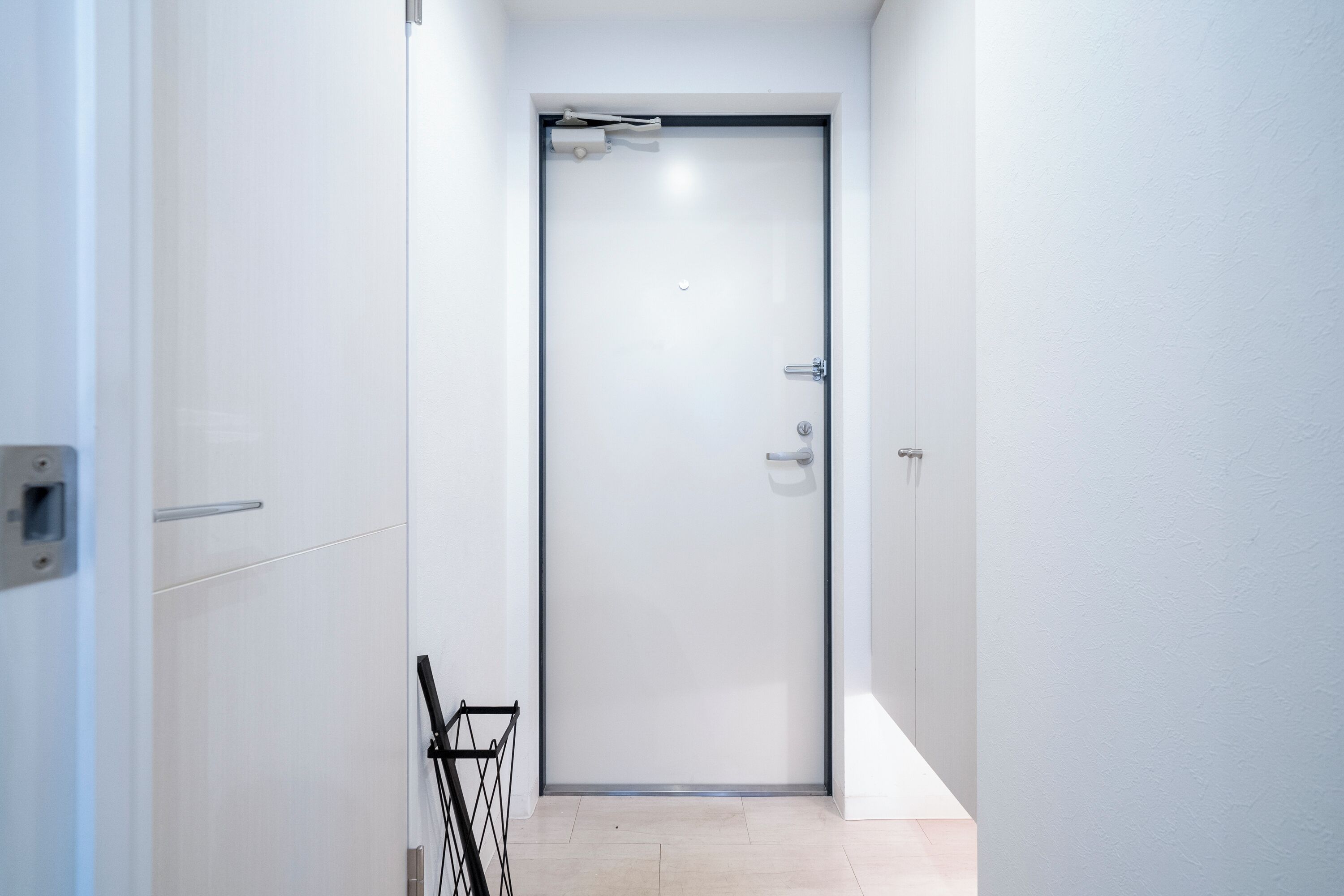 A narrow hallway with a white door, a small trash bin, and a light switch on the wall.