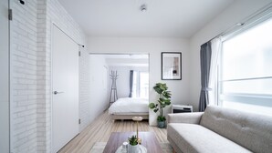 A modern, well-lit bedroom with a bed, bedside table, and a large window. - EVARIA (Sapporo)