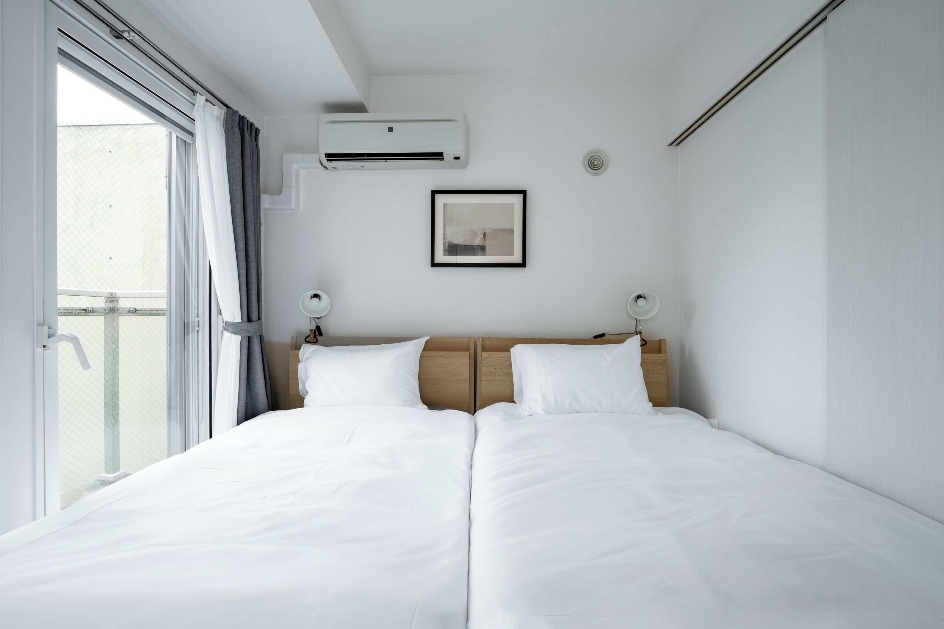 A hotel room with a large bed, an air conditioning unit, a framed picture on the wall, and a window with curtains.