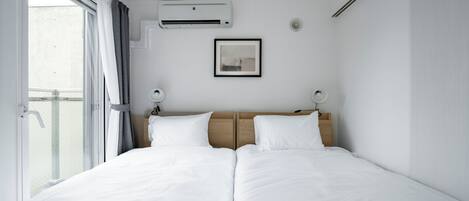 A hotel room with a large bed, an air conditioning unit, a framed picture on the wall, and a window with curtains.
