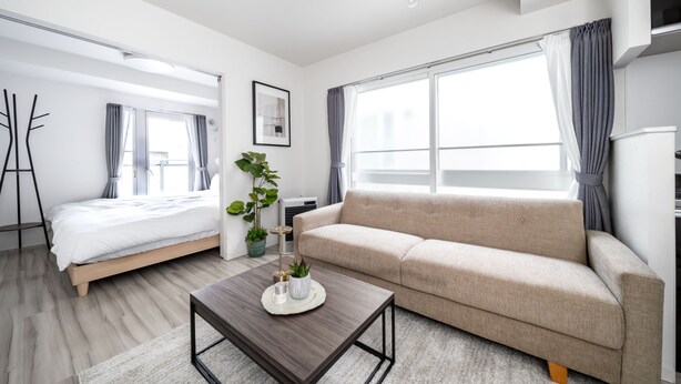 A modern hotel room with a bed, a sofa, a coffee table, and a large window with curtains. - EVARIA (Sapporo)