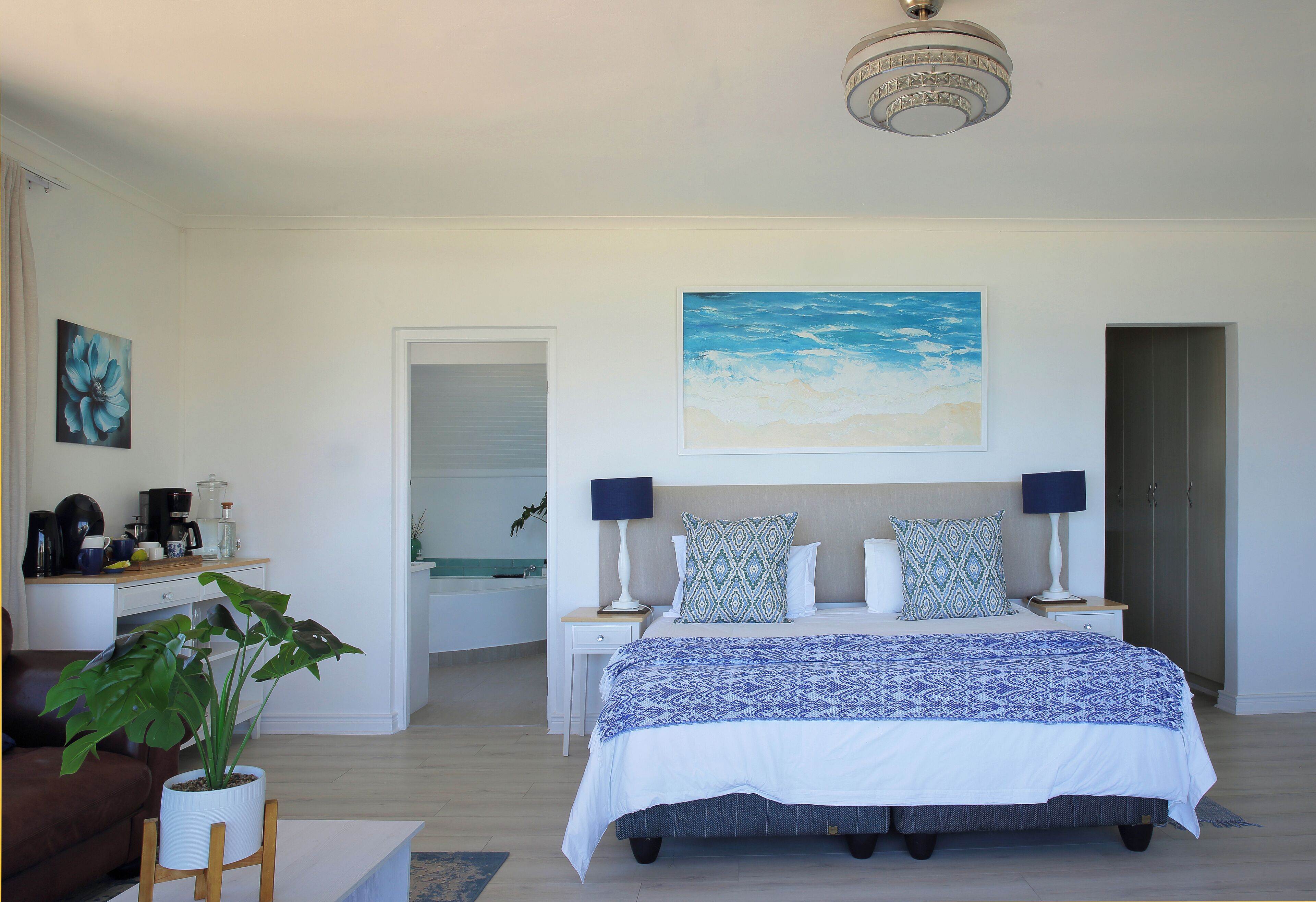 Quarto com cama, mesas de cabeceira, luminária, planta e um quadro na parede.