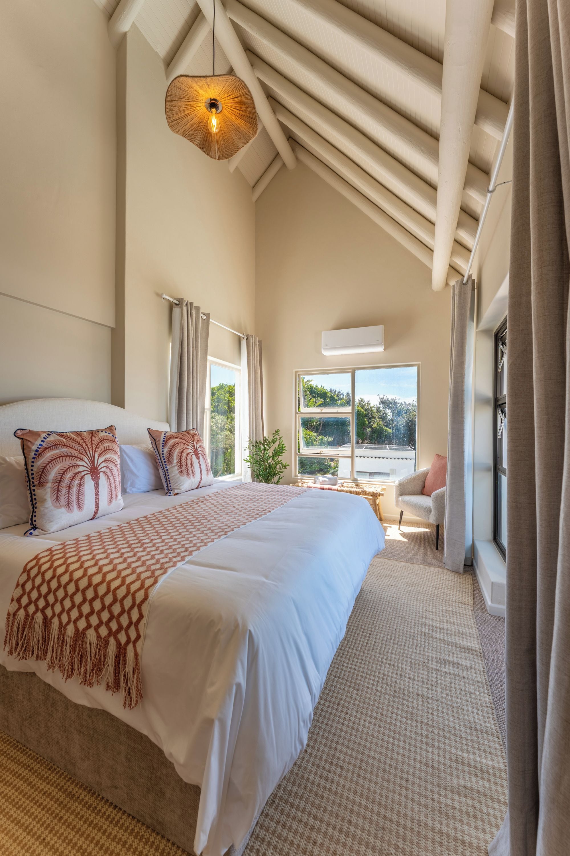 Un dormitorio con una cama grande, un ventilador de techo, una ventana con cortinas y vistas al exterior.