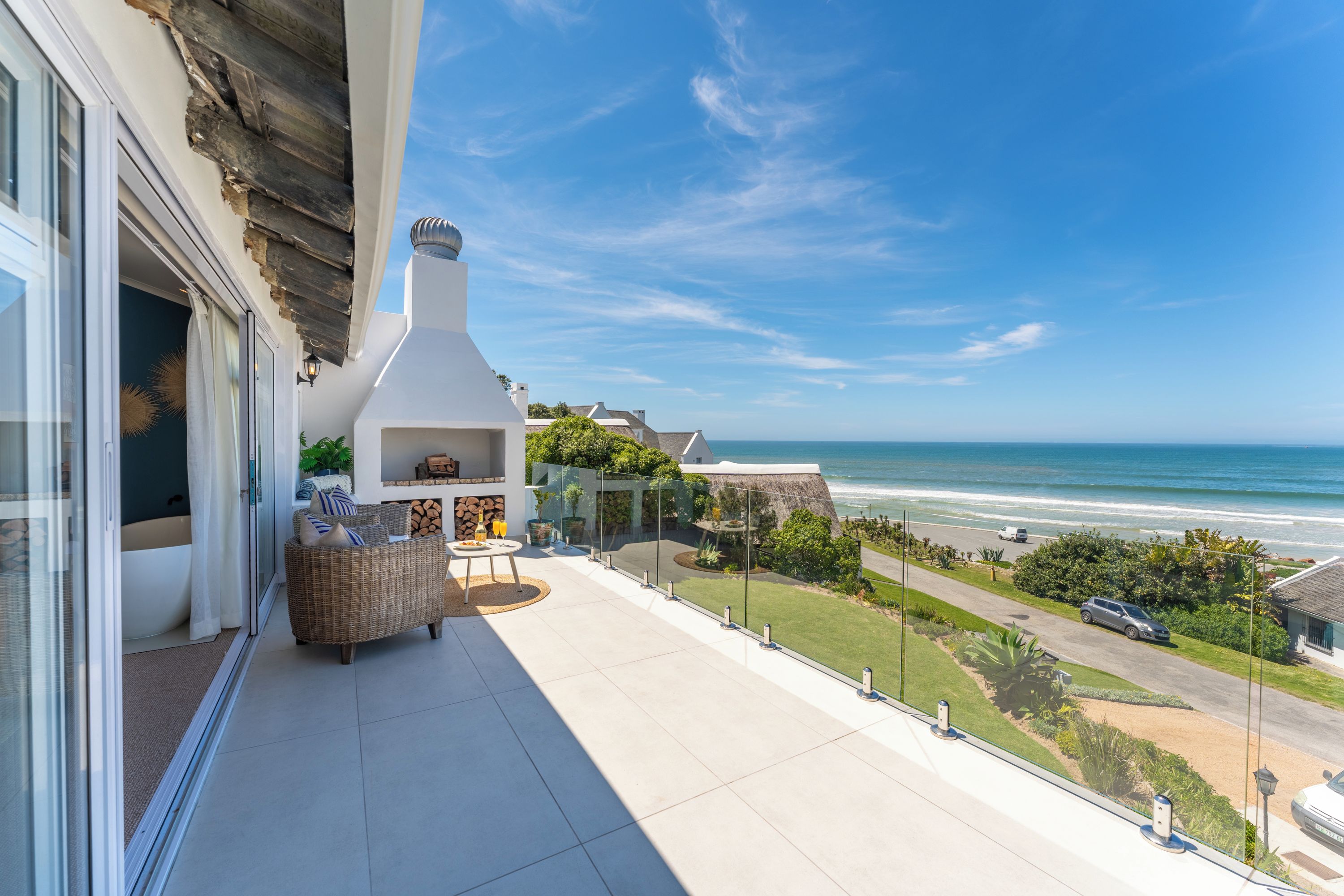 Un balcón con vista al océano, un comedor con mesa y sillas, y una chimenea blanca grande.