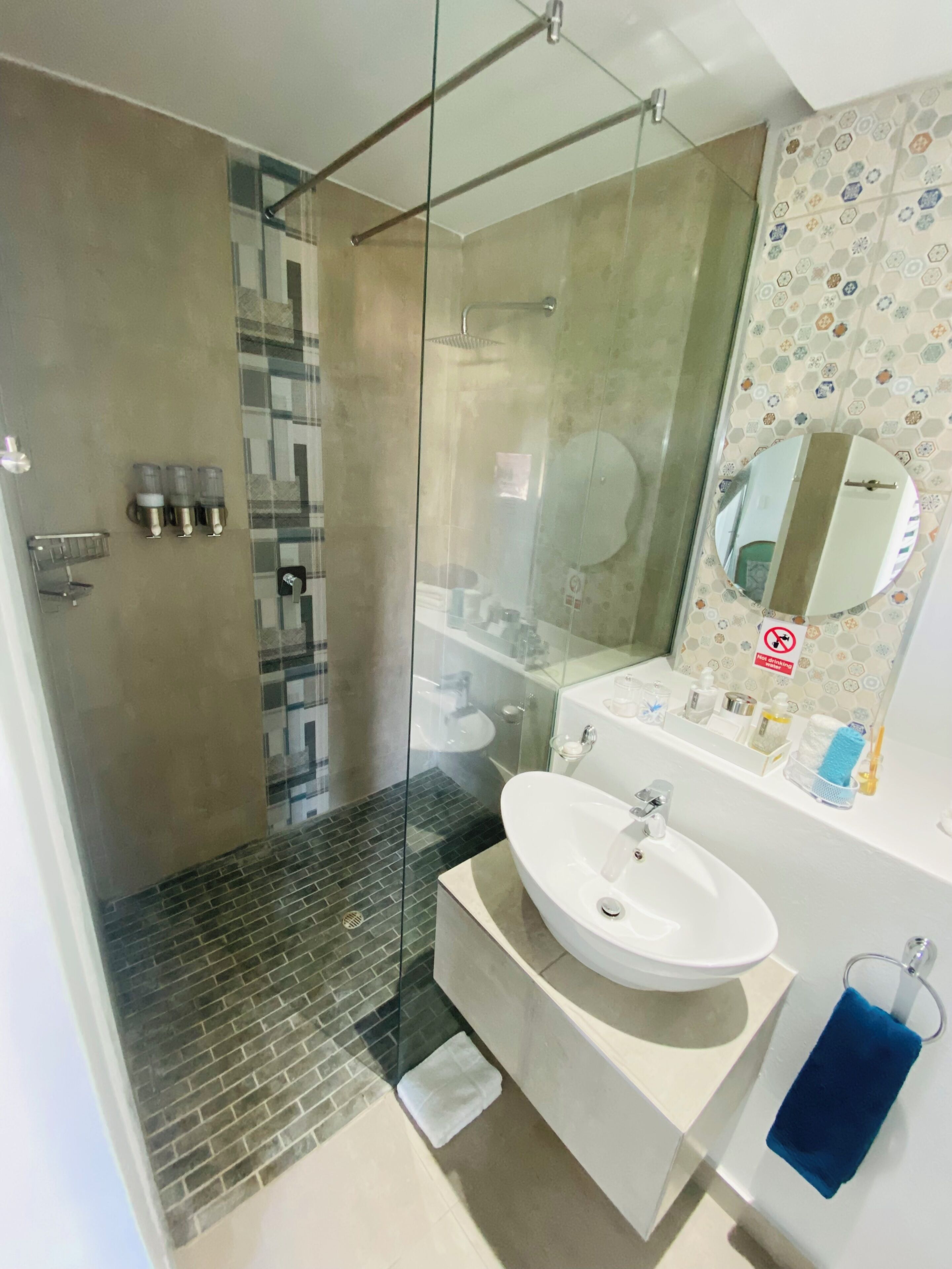 A modern bathroom with a glass-enclosed shower, a white sink, and a mirror with a hexagonal tile backsplash.