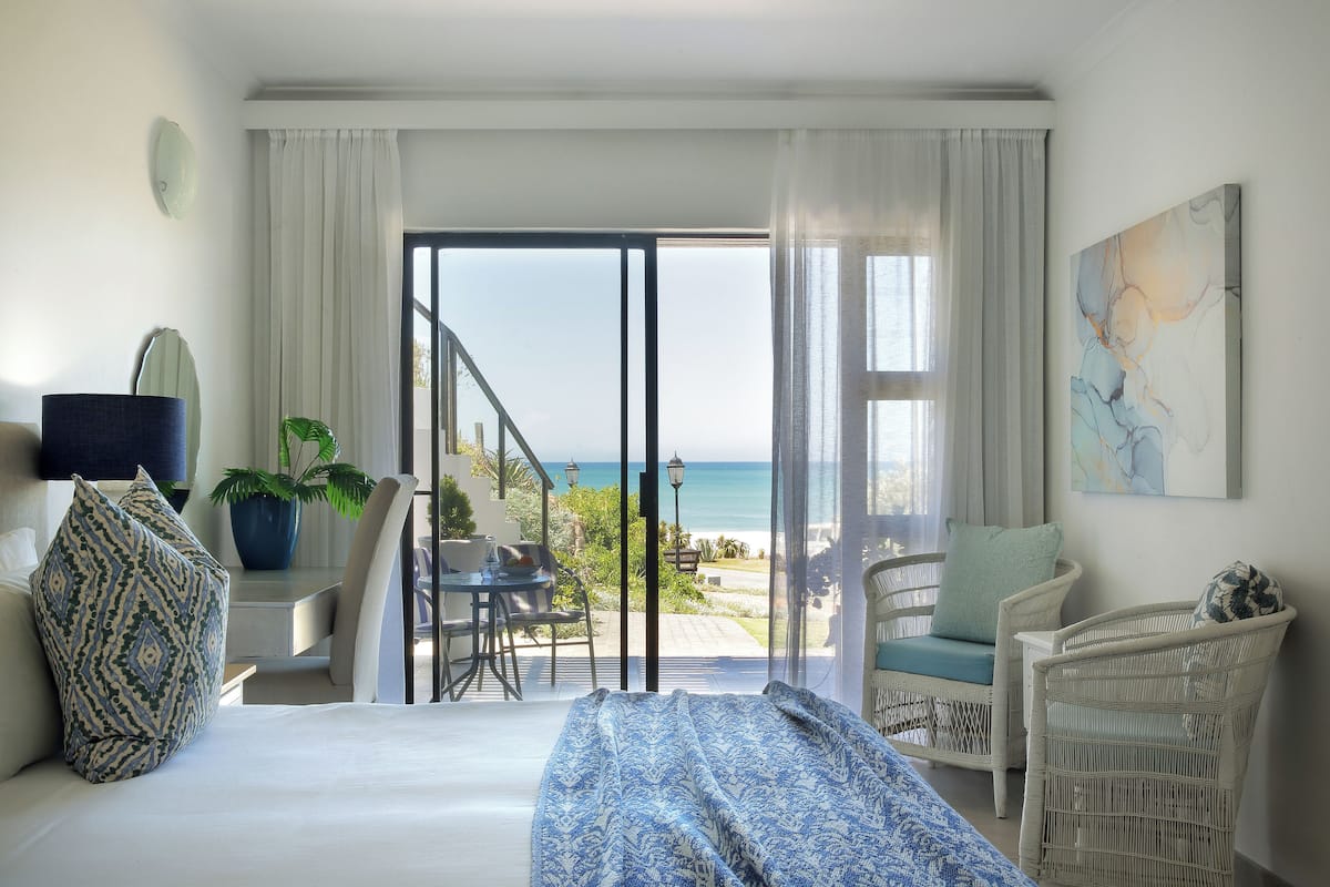 Un dormitorio con cama, una silla, una mesa y vista al océano.