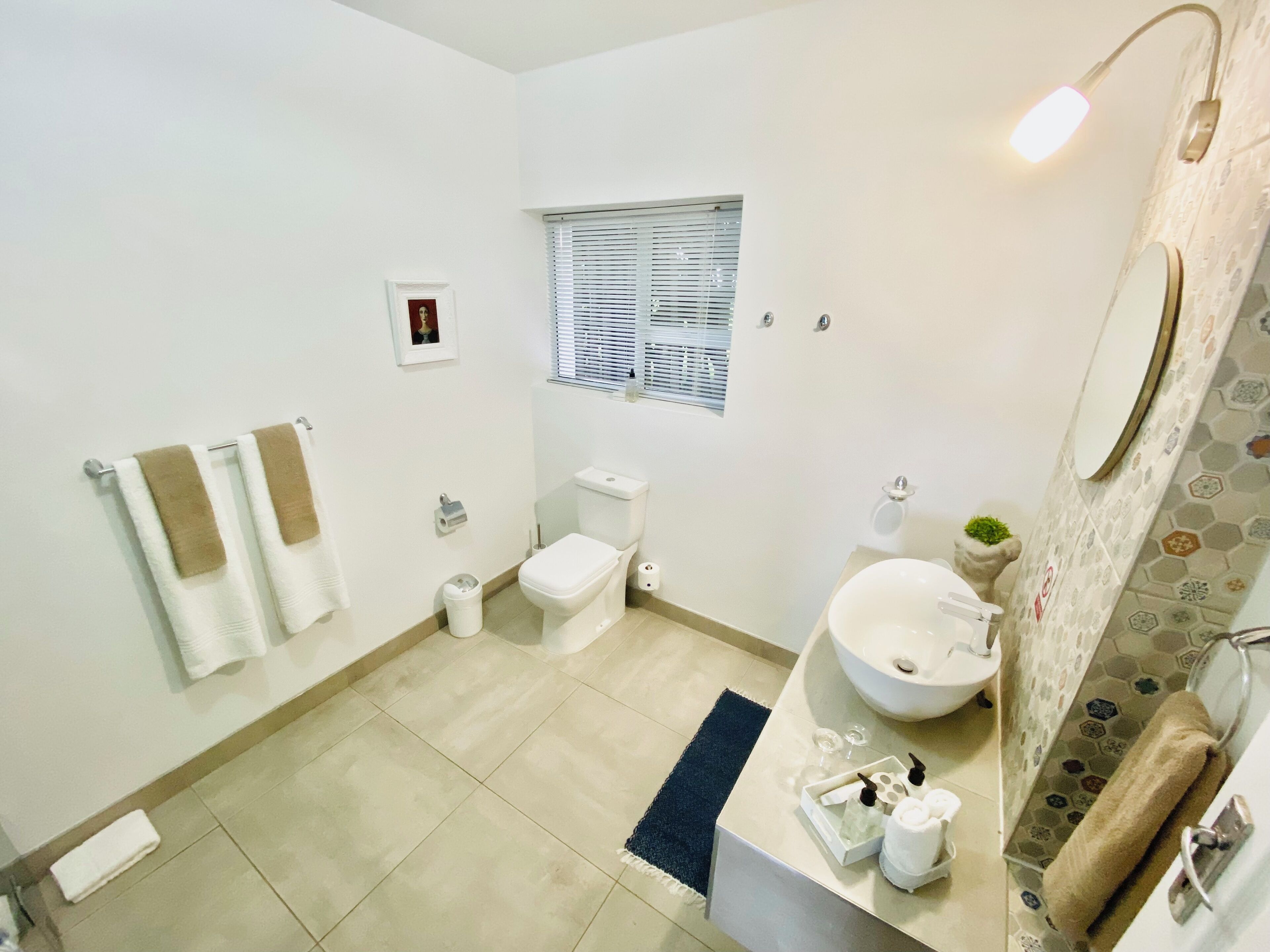 A modern bathroom with a toilet, sink, and mirror. There are towels on the wall and a small window above the toilet.