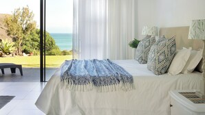 A bedroom with a large bed, a nightstand, a view of the ocean, and a sliding glass door leading to a balcony.