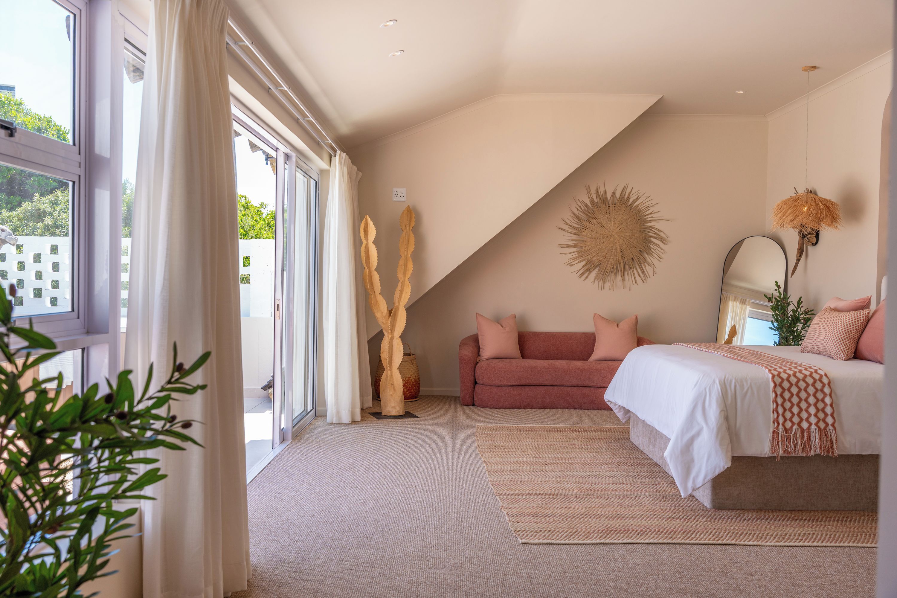 A bedroom with a large window, a sofa, a bed, and a decorative wall piece.