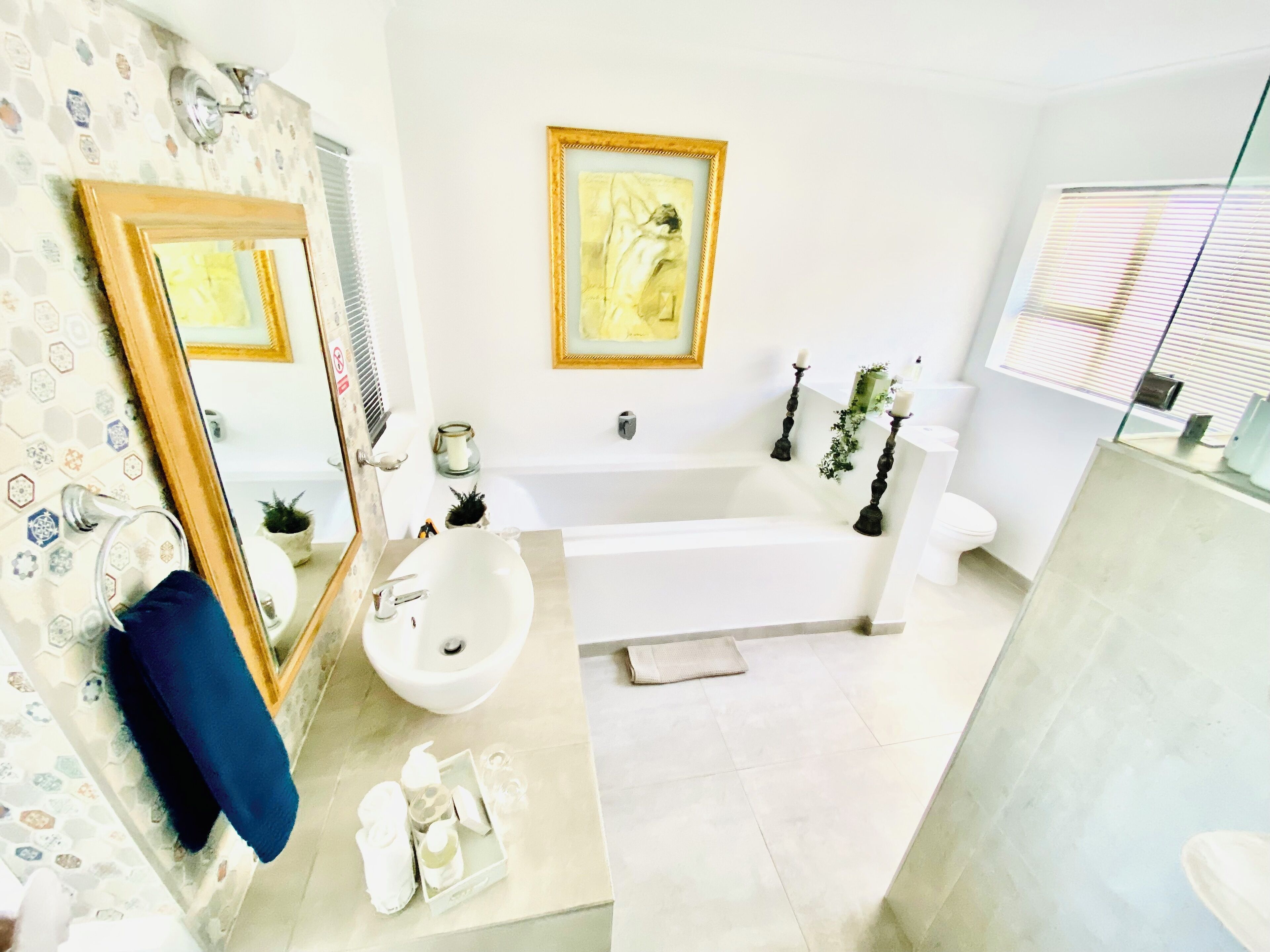Een badkamer met een grote spiegel, een bad, een wastafel en een toilet. Daarboven, boven het bad, hangt een fotolijst aan de muur.
