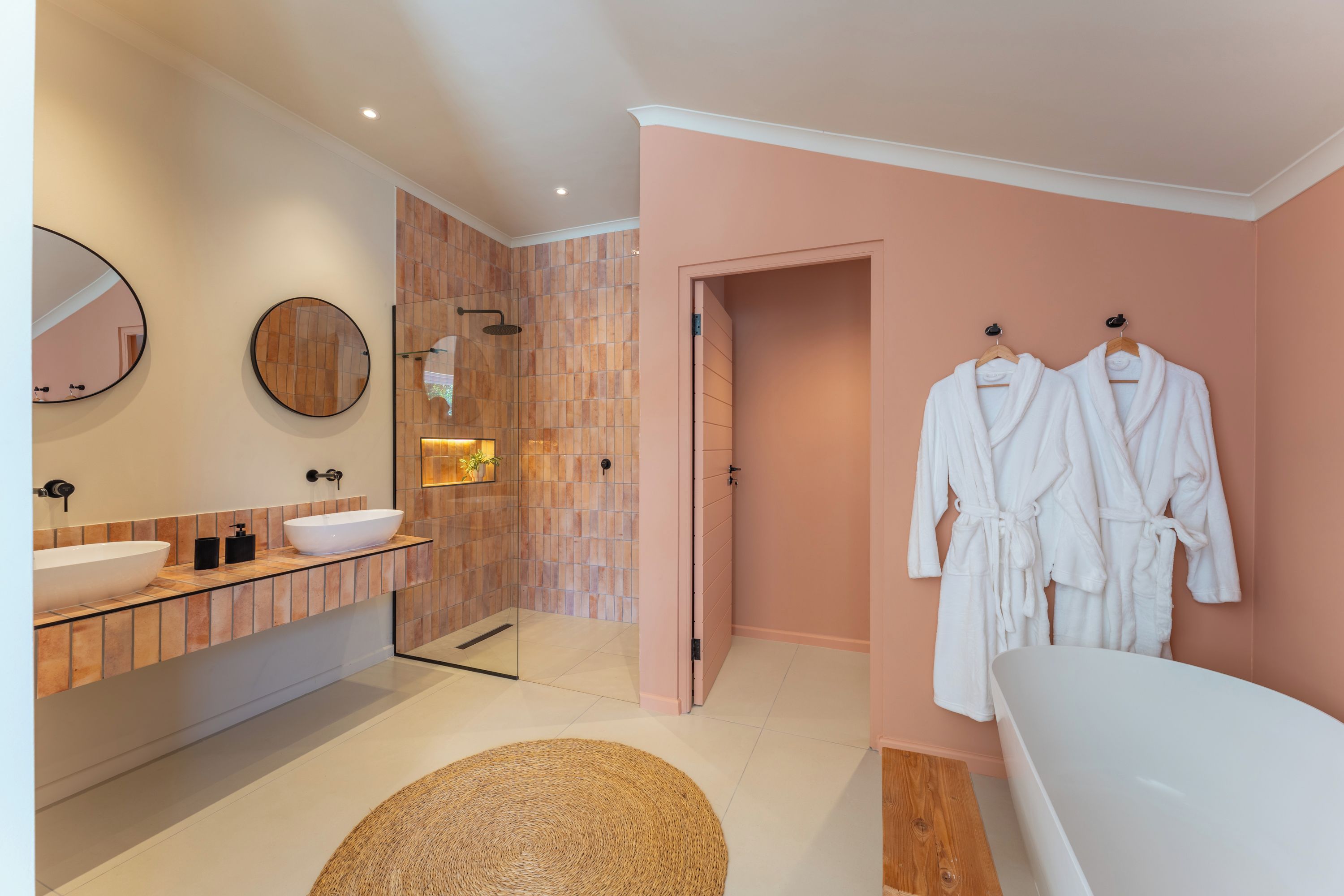 A modern bathroom with a large mirror, a round mirror, a white bathtub, and two white robes hanging on hooks.