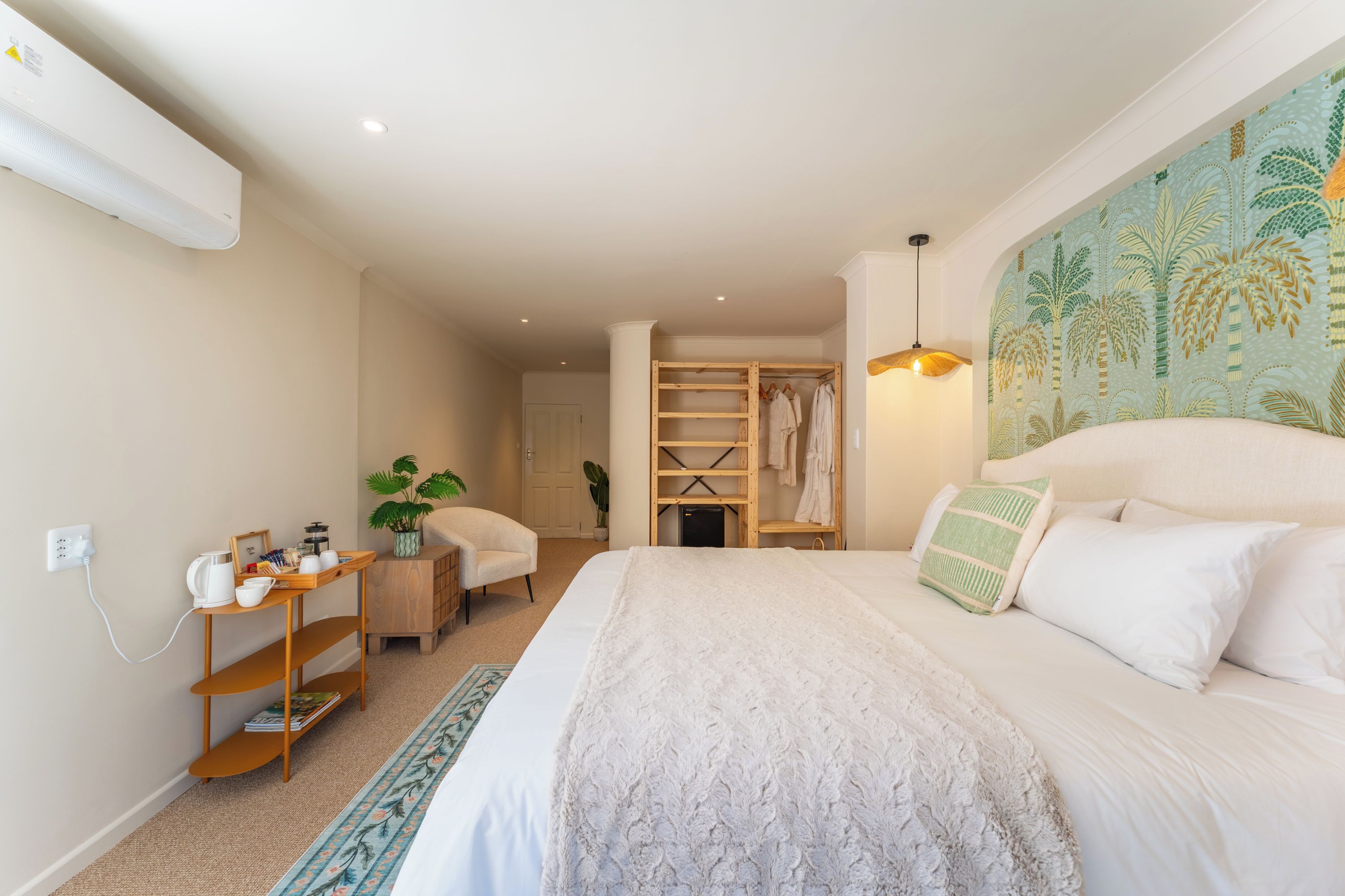 A bedroom with a bed, bedside table, and a wardrobe with hanging clothes.