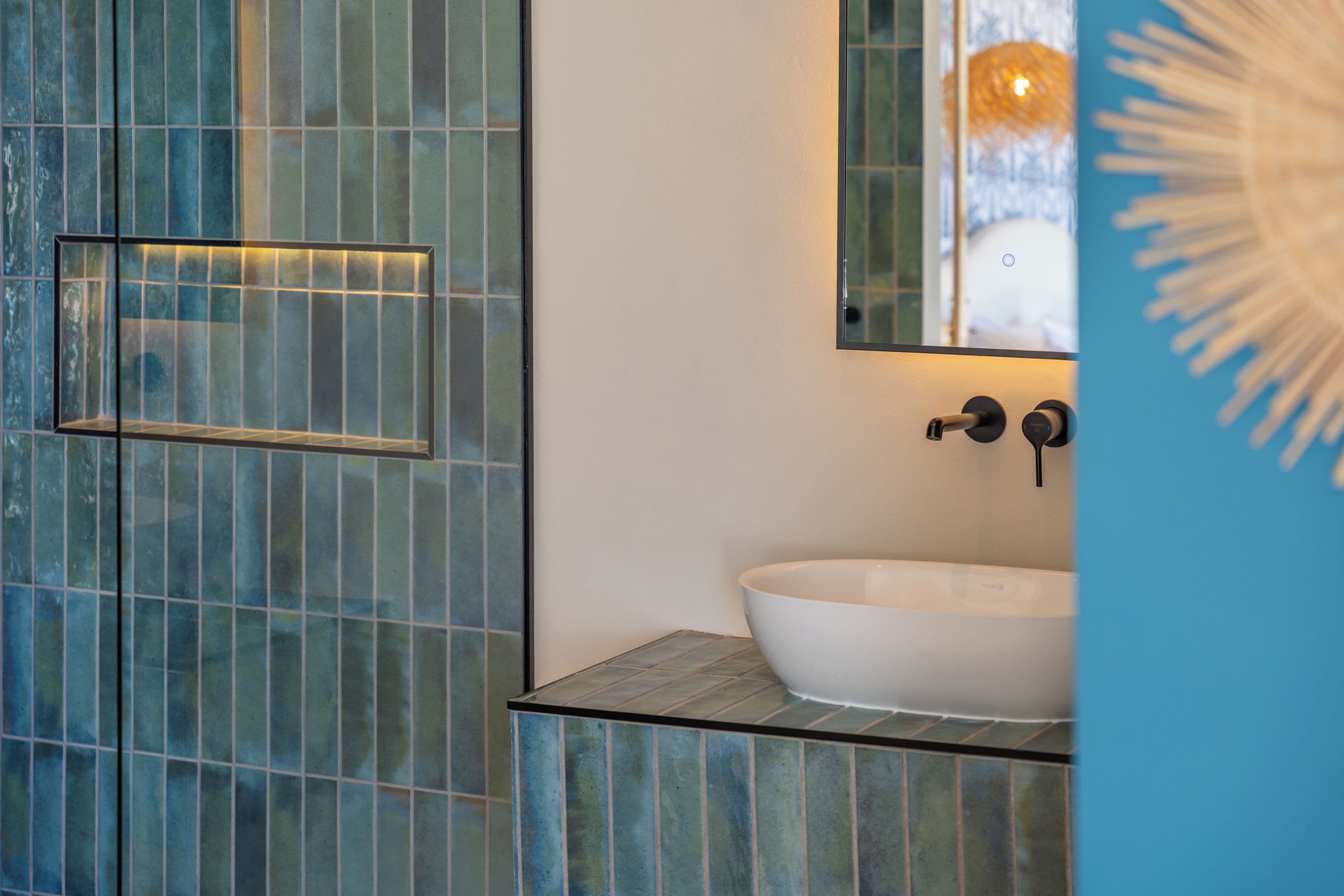 A bathroom with a glass-tiled wall, a white sink, and a mirror above it.